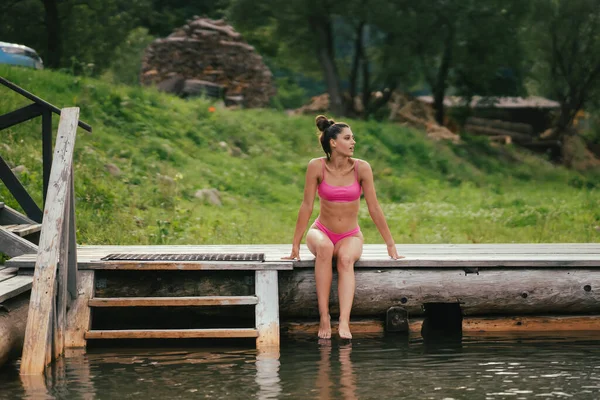 Mooie vrouw in bikini op de houten pier naast een water — Stockfoto