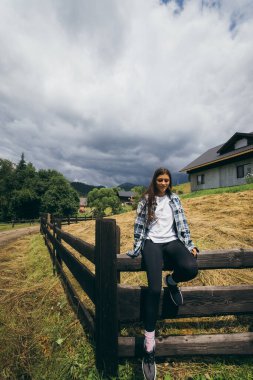 Çitin üzerinde oturan genç ve çekici beyaz bir kadın.