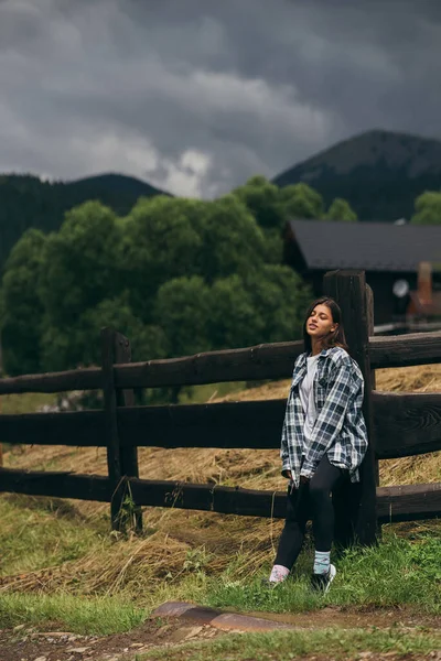 Genç, çekici, beyaz bir kadın çitin yanında duruyor.