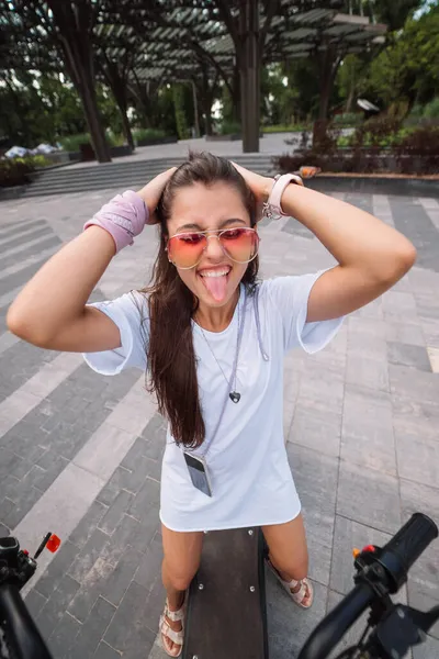 Young beautiful woman sitting on electric scooter and showing tongue — Stock Photo, Image