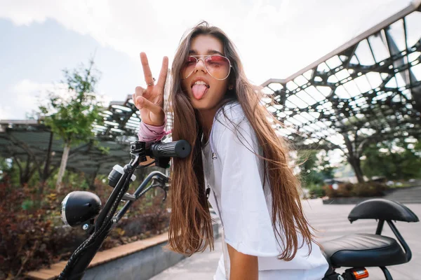 Jovem bela mulher sentada em scooter elétrico e mostrando língua — Fotografia de Stock