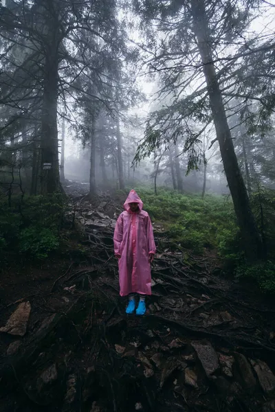 Mujer joven en un impermeable camina por el bosque bajo la lluvia — Foto de Stock