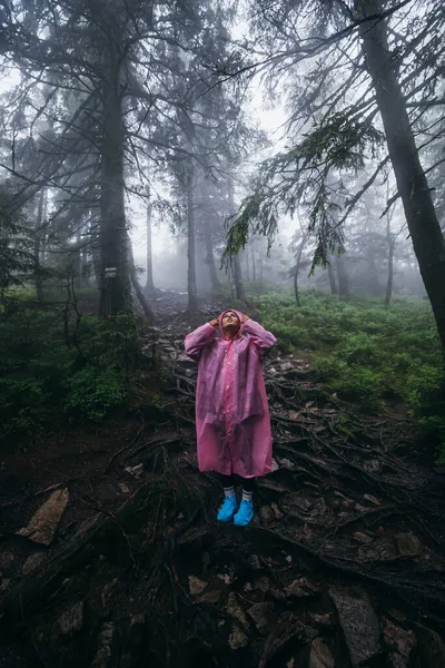 穿着雨衣的年轻女子在雨中穿过森林 — 图库照片