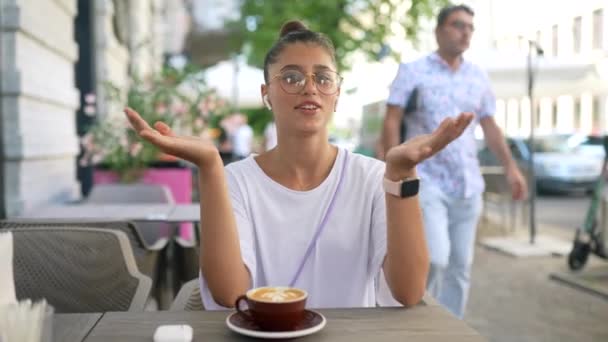 Chica está sentado en la cafetería al aire libre y habla con la cámara — Vídeo de stock