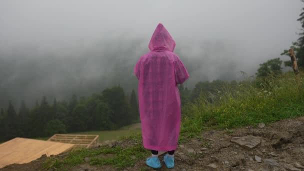 Attractive hiker girl in a pink raincoat stands on a mountain — Stock Video