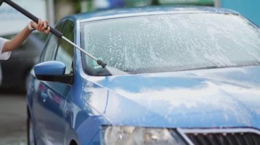 Araba yıkamada mavi araba yıkayan genç bir kadın.