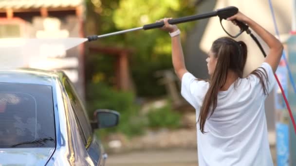 Молодая женщина моет синюю машину на автомойке — стоковое видео