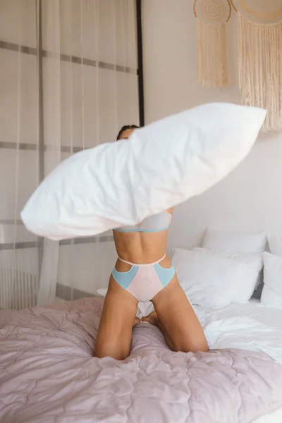 Жінка в нижній білизні грає з подушкою на ліжку — стокове фото
