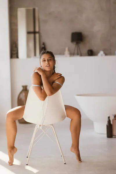 Meisje in lingerie zit op een stoel en kijkt naar de camera — Stockfoto
