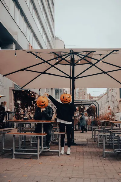 Guy and girl with pumpkin heads in a street cafe — Stock Photo, Image