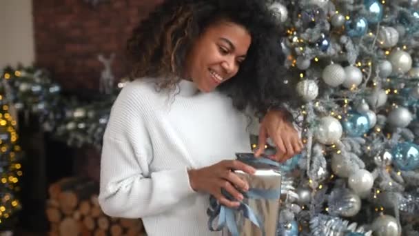 Sonriente joven afroamericana abre caja con regalo de Navidad. — Vídeos de Stock