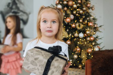 Sevimli küçük kız Noel ağaçlarının arka planında bir hediye tutuyor.