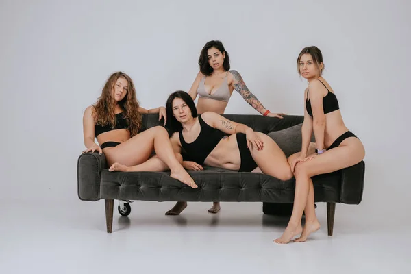 Diversos modelos con ropa interior cómoda posando en un sofá grande —  Fotos de Stock