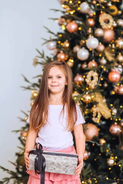 Charmantes kleines Mädchen hält ein Geschenk auf einem Hintergrund von Weihnachtsbäumen — Stockfoto