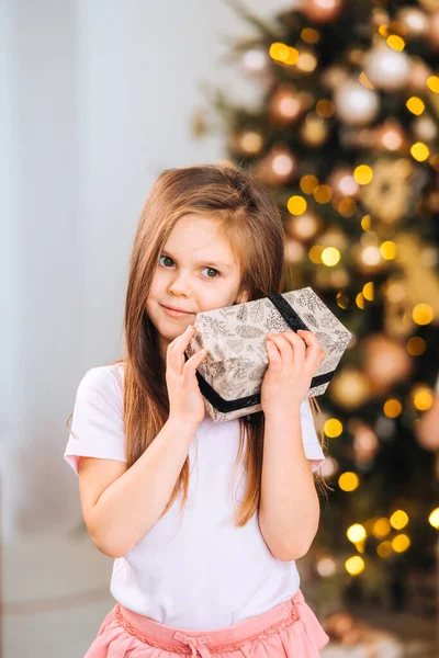 Charmantes kleines Mädchen hält ein Geschenk auf einem Hintergrund von Weihnachtsbäumen — Stockfoto