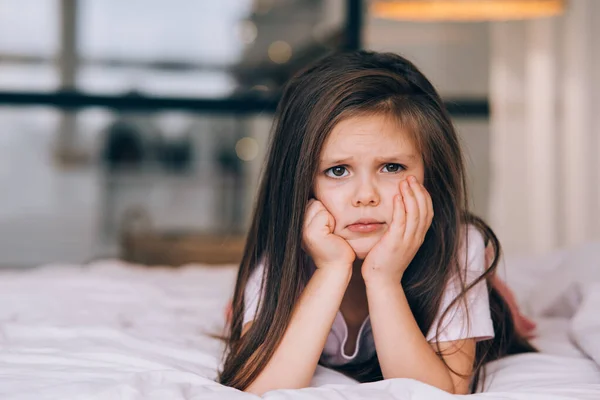 Cute little girl with a sad face lying on the bed — Stock Photo, Image