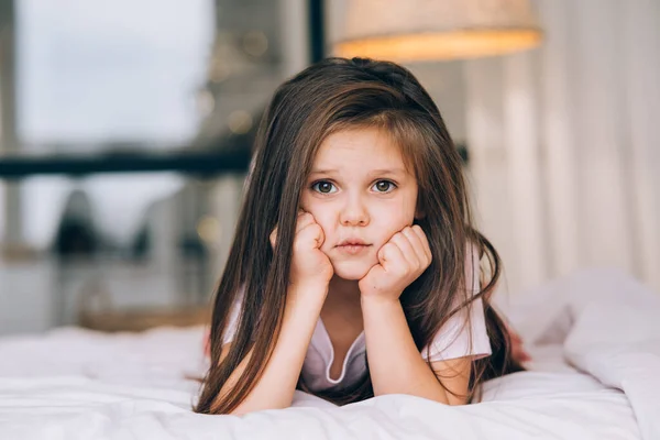 Menina bonito com um rosto triste deitado na cama — Fotografia de Stock