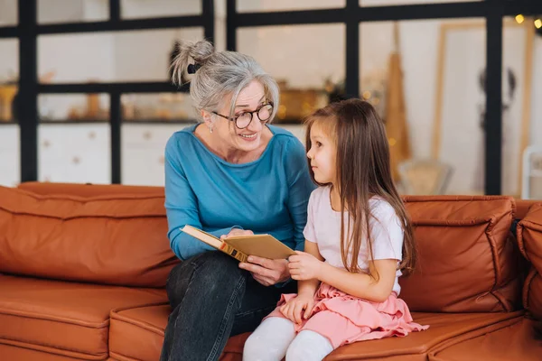 Nette ältere Großmutter liest Enkelin Geschichte vor. — Stockfoto