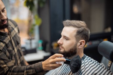 Usta kalan saçı bir fırçayla müşteriden alıyor.