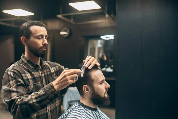 Cheerful young bearded man getting haircut by hairdresser at barbershop — Stock Photo, Image