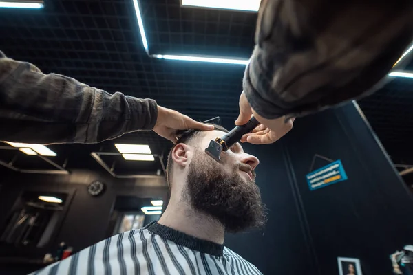 O barbeiro trabalha com um cortador de barba. Hipster cliente recebendo corte de cabelo. — Fotografia de Stock