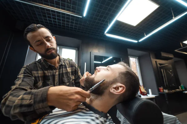Парикмахер стрижет бороду с помощью расчески и ножниц — стоковое фото