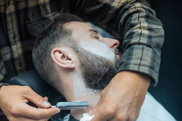 Joven barbudo afeitado por peluquero en la peluquería — Foto de Stock