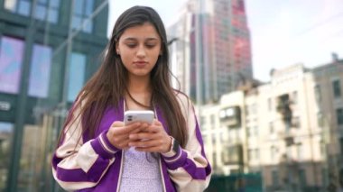Sokaktaki mutlu kadın akıllı telefon kullanıyor ve kameraya bakıyor.