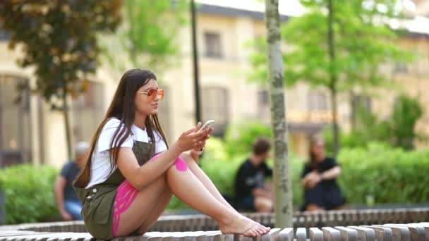Csinos fiatal nő használja mobiltelefon app a városi parkban — Stock videók