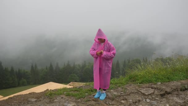 魅力的なハイカーの女の子でピンクのレインコートは山の上に立つ — ストック動画