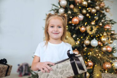 Sevimli küçük kız Noel ağaçlarının arka planında bir hediye tutuyor.