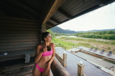 Pembe mayo giymiş, elinde kahve fincanı olan mutlu bir kadının yan görüntüsü.