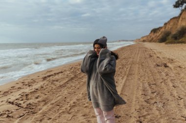 Soğuk sonbahar sahilinde kameraya poz veren genç bir kadın.