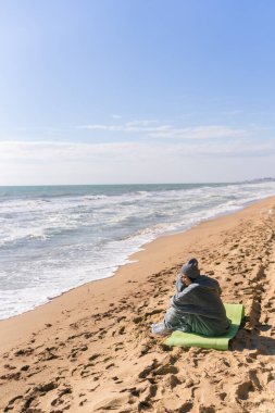 Soğuk sonbahar kumsalında oturan kalın elbiseli güzel bir kadın..