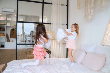 Yatak odasında yastıklarla oynayan iki küçük kız.