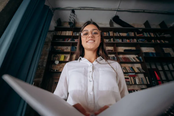 Junge Frau hält ein aufgeschlagenes Buch in der Hand und blickt in die Kamera — Stockfoto