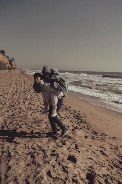 Homem carrega sua namorada nas costas, casal se divertindo na praia — Fotografia de Stock