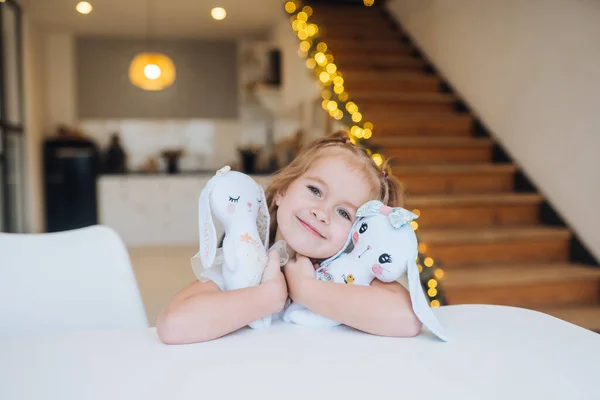 Kleines lächelndes Mädchen umarmt Lieblings-Teddybär am Tisch — Stockfoto