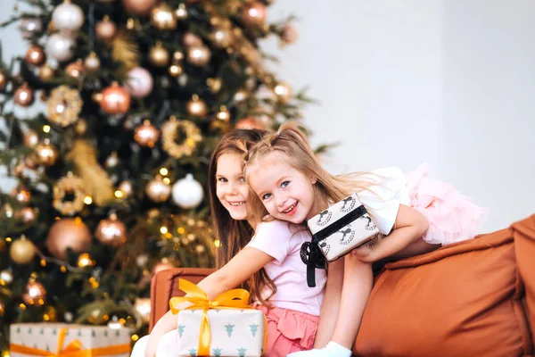 Zwei kleine Mädchen spielen mit Neujahrsgeschenken am Baum auf dem Sofa. — Stockfoto