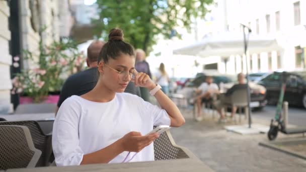 Beautiful young woman sitting in street cafe using a smartphone — Stock Video