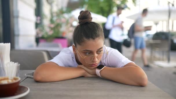 Скучная, равнодушная девушка за столом в уличном кафе — стоковое видео