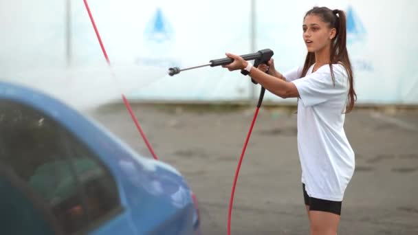 Araba yıkamada mavi araba yıkayan genç bir kadın. — Stok video