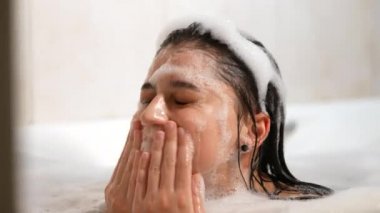 Rahat kadın banyoda tenine köpükle dokunuyor..