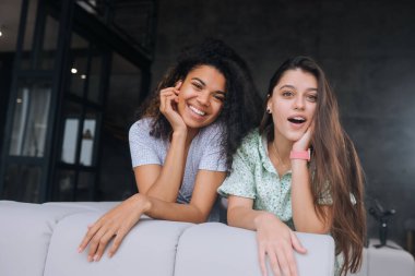 İki kız kanepede oturur, kameralara bakar ve gülümserler.