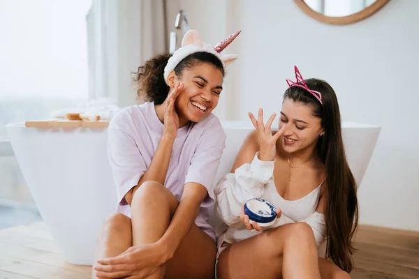 Две девушки в ванной играют с кремом для лица — стоковое фото