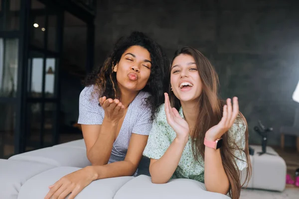 Duas meninas sentam-se na parte de trás do sofá, olham para as câmeras e sorriem — Fotografia de Stock