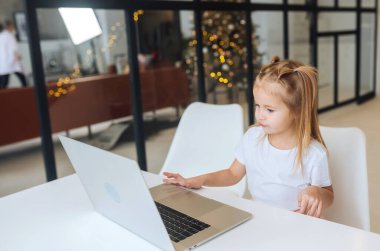 Tablet bilgisayar kullanan küçük kız masada oturuyor.