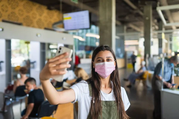 Молодая женщина в розовой маске использует смартфон в помещении. — стоковое фото