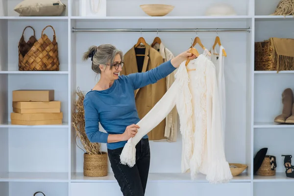 Starší žena při výběru bílého svetru doma — Stock fotografie