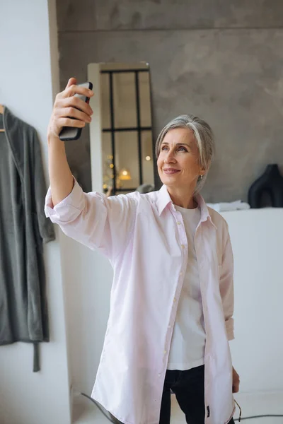 Cheerful confident excited dreamy elderly female taking selfie — Stock Photo, Image